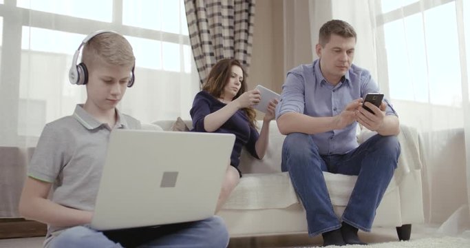 Family of three people uses gadgets and does not communicate. Сoncept of Internet addiction people. Dolly shot 4K