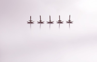Five drawing pins, reflected in a white surface