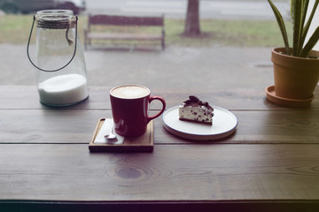 Cappuccino in a red mug with a cake on a wooden table