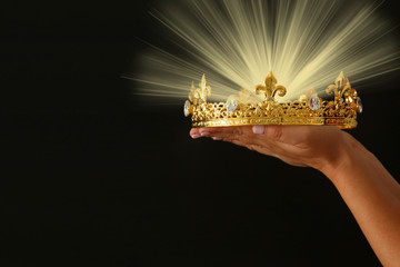 Woman's hand holding a crown for show victory or winning first place over black background with...