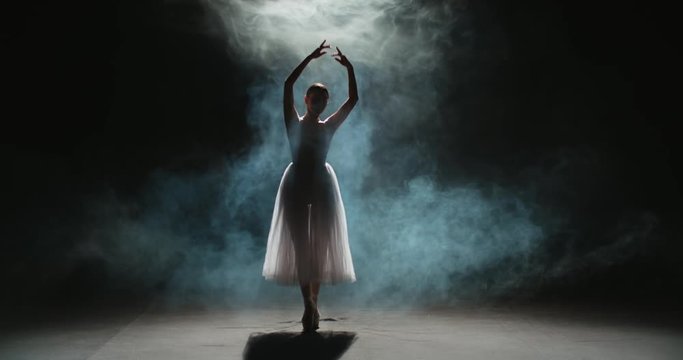 4K video footage of silhouette of beautiful female ballet dancer in white tutu on black background, slow motion