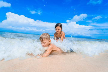 Cute boy and girl having fun on the sunny tropical beach. Lying on sand, wonderful waves around them. View from above. Vibrant color concept, copy space