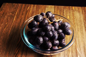 High angle shot of fruit bowl full of violet purple bunch of  grapes on wooden cabinet