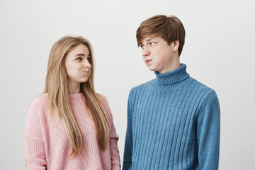 Waist up portrait of young female and male wearing knitted colourful sweaters having discontent...