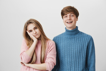 Family and relationships concept. Studio shot of irritated blonde girl resting her head on hand, because she is tired of her younger brother`s jokes and behaviour. Body language and face expression.