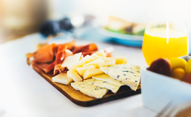 Prosciutto, parmesan on wooden board on kitchen table, blur concept, spanish breakfast with serrano jamon and gorgonzola cheese closeup, traditional food on restaurant or cafe