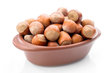 hazelnuts in clay bowl on white background