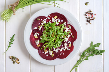 Beetroot carpaccio with rucola leaves and pumpkin seeds on wooden white background.