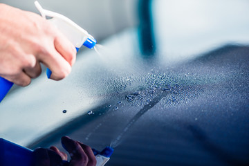 Close-up of hand spraying cleaning substance on the surface of a blue car at auto wash