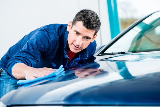 Young man using an absorbent soft towel for drying and polishing the surface of a clean blue car