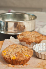 Close up of two, freshly baked, homemade, mini peach streusel coffee cakes, cooling in forming tins on parchment paper on wood cutting board and spring pan