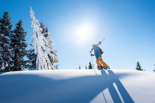 Full length shot of a male skier on top of the mountain with his skis on his shoulder on a sunny winter day sunlight nature recreation skiing resort lifestyle sportive concept