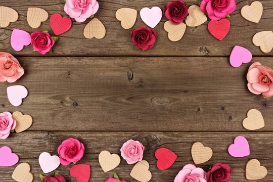 Valentines Day frame of wooden hearts and paper roses against a rustic wood background with copy space.