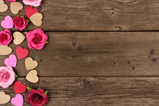 Valentines Day side border of wooden hearts and paper roses against a rustic wood background with copy space.