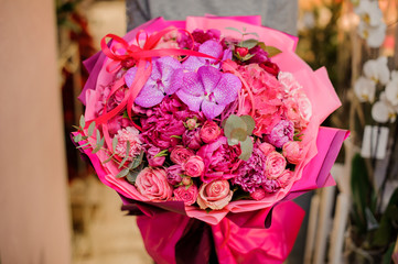 girl holds a bouquet of peonies, roses and orchids decorated with eucalyptus