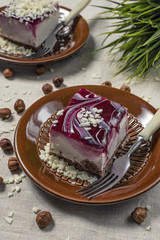 A piece of vanilla cake with chocolate base and cherry glaze decorated with some pieces of white...