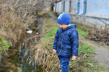 the boy in a blue jacket looks at the water on the street