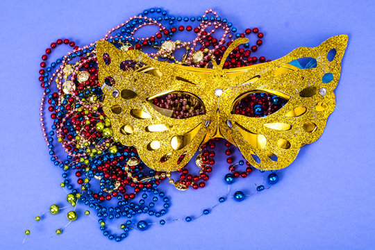 Gold carnival mask with colored beads on violet background
