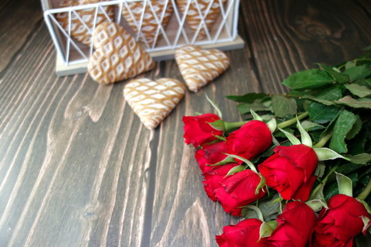 Bouquet of fresh red roses and sweet heart-shaped cookies on wooden background, Valentine`s Day concept