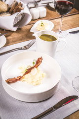 Cream of sorrel and green vegetables soup with quail egg, sour cream, mashed potatoes and crispy bacon served in a jug in a restaurant