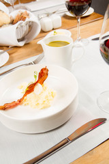 Cream of sorrel and green vegetables soup with quail egg, sour cream, mashed potatoes and crispy bacon served in a jug in a restaurant