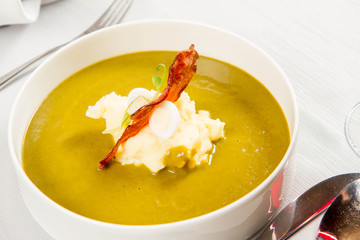 Cream of sorrel and green vegetables soup with quail egg, sour cream, mashed potatoes and crispy bacon served in a restaurant