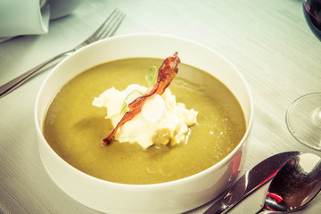 Cream of sorrel and green vegetables soup with quail egg, sour cream, mashed potatoes and crispy bacon served in a restaurant