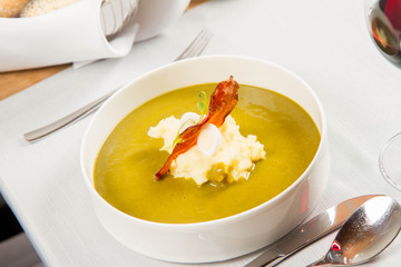 Cream of sorrel and green vegetables soup with quail egg, sour cream, mashed potatoes and crispy bacon served in a restaurant