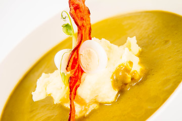 Cream of sorrel and green vegetables soup with quail egg, sour cream, mashed potatoes and crispy bacon on a white background