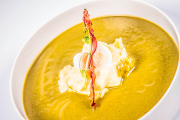 Cream of sorrel and green vegetables soup with quail egg, sour cream, mashed potatoes and crispy bacon on a white background