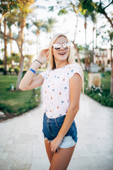 Naklejka premium Relaxed happy smile young woman in sunglasses on terrace of hotel on palms background. Summer vocation