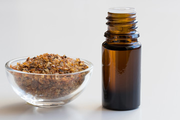 A bottle of myrrh essential oil with myrrh resin on a white background
