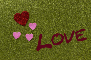 Red and pink sparkly hearts on green background that says Love, with copy space