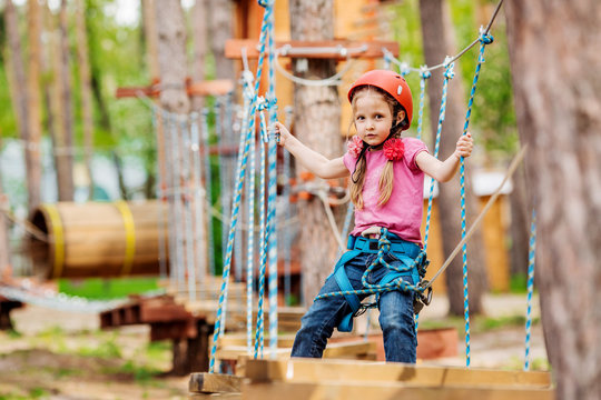 baby girl with climbing gear  in an adventure park are engaged in rock climbing or pass obstacles on the rope road.