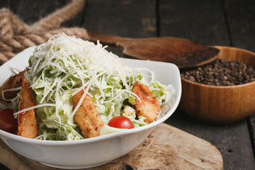 Caesar salad with chicken and lettuce in white bowl on wooden table