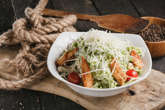Caesar salad with chicken and lettuce in white bowl on wooden table