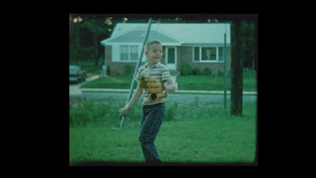 1960 7 year old blond boy playing catch with baseball in suburban backyard
