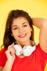 Beautiful young woman in red t shirt listen music over yellow background with copy space