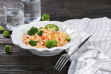 Plate with rice pilaf and broccoli on wooden table