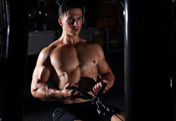 Obraz na płótnie Canvas Young man training on exercise machine in gym