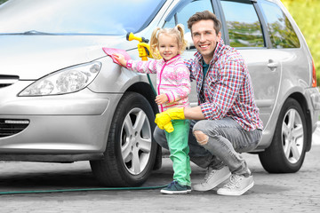Man with his little daughter washing car outdoors