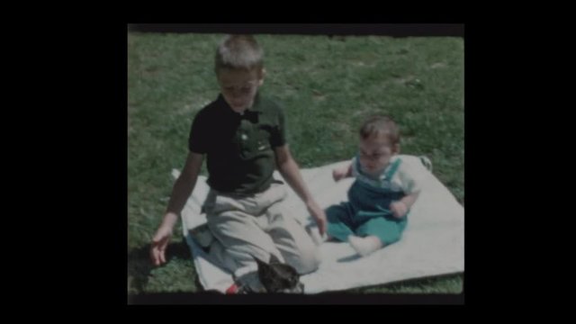 1960 Young boy and baby brother play with dog