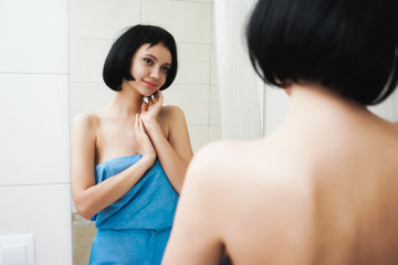 Fototapeta na wymiar girl with short hair after shower looks in the mirror and cute smile