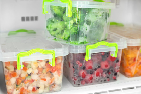 Containers with frozen berries and vegetables in freezer, closeup