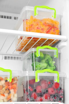 Containers with frozen berries and vegetables in freezer, closeup