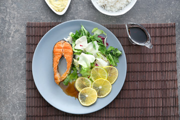 Tasty rainbow trout steak with garnish and sauce on plate, top view