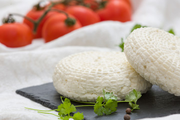 Closeup of round white homemade cheese - traditional milk creamy dairy product served with herbs and tomatoes on vintage black board. Rustic style.