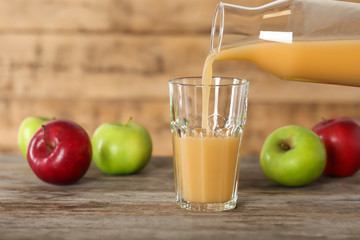 Pouring apple juice from bottle into glass on table