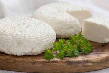 Sliced round white homemade cheese - traditional milk creamy dairy product on vintage wooden board. Rustic style.