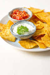 Snack for a party, chips with tortilla, nachos with sauces: salsa with tomatoes, sour cream. Mexican food. Bright white background. Copy space